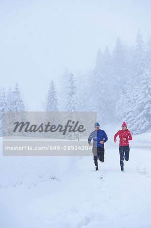 Female and male runners running in falling snow, Gstaad, Switzerland