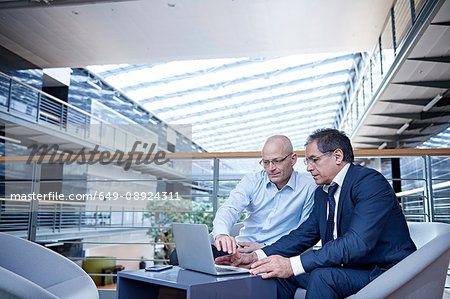 Two mature businessmen looking at laptop in meeting on office balcony