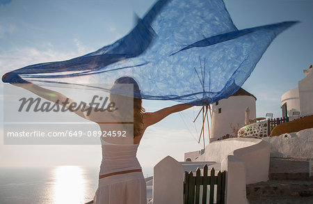 Woman arms raised holding kaftan looking away at view of sea, Santorini, Cyclades, Greece
