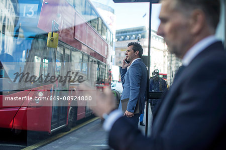 Businessman waiting at bus stop using smartphone, London, UK