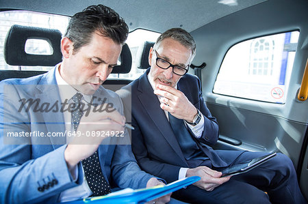 Two businessmen looking at paperwork in taxi cab