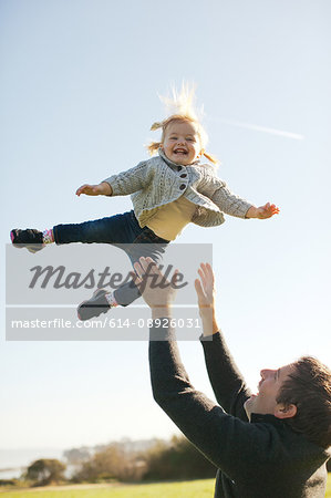 Female toddler thrown mid air by father against blue sky