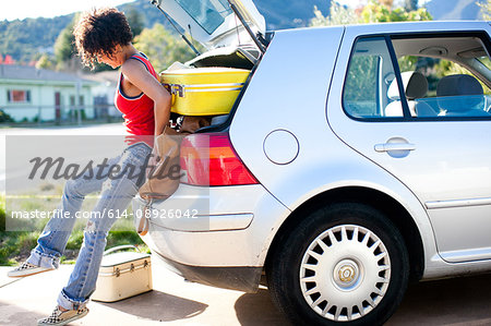 Woman struggling to push luggage into car boot