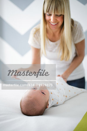 Mid adult woman swaddling baby son on bed