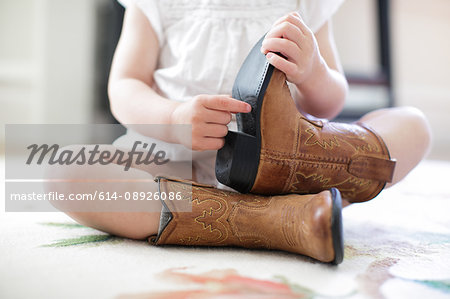 Neck down view of female toddler sitting on floor wearing cowboy boots