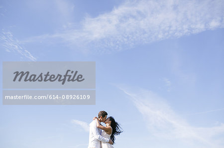 Romantic couple kissing against vast blue sky