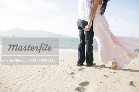 Neck down view of romantic couple  hand in hand on beach