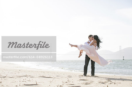 Romantic man carrying girlfriend in arms on beach, San Francisco Bay, USA