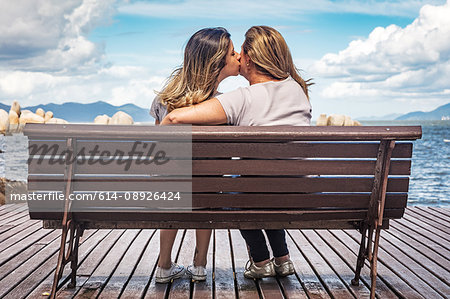 Rear view of mother and daughter on park bench kissing