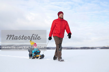 Father pulling sons along on sledge in snow covered landscape