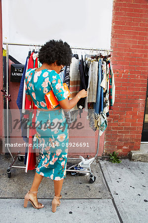 Rear view of young female fashion blogger with afro hair looking at sidewalk clothes rail, New York, USA