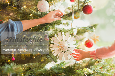 Mother and daughter hanging snowflake ornament on Christmas tree