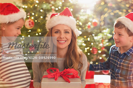 Portrait smiling mother in Santa hat receiving Christmas gift from daughter and son