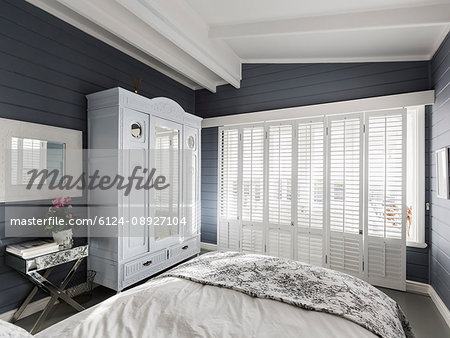 Luxury home showcase bedroom with white wood shutters and vaulted ceiling