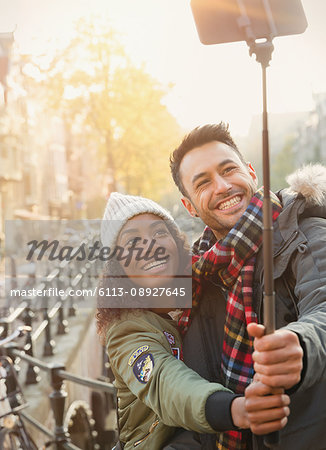 Smiling young couple taking selfie with selfie stick on urban street