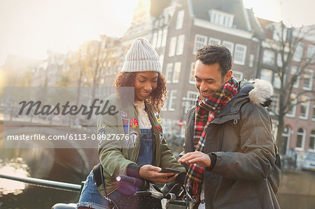 Young couple with bicycle using cell phone on urban bridge, Amsterdam