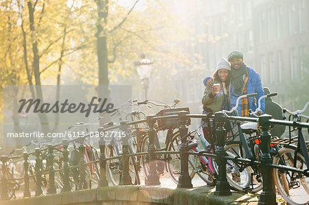Portrait smiling young couple drinking coffee along bicycles on sunny urban autumn bridge, Amsterdam
