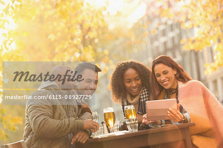 Smiling friends drinking beer and taking selfie with digital tablet at autumn sidewalk cafe