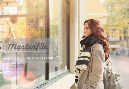 Smiling young woman window shopping at urban storefront