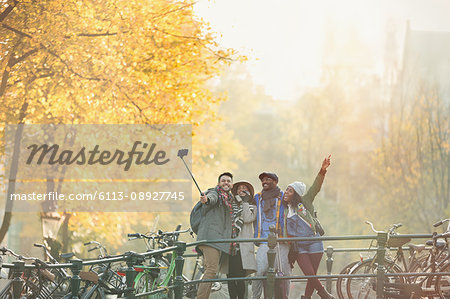 Playful young friends taking selfie with selfie stick on urban autumn bridge, Amsterdam