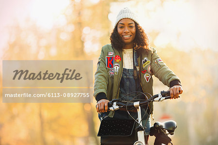 Portrait smiling young woman with bicycle in front of autumn trees