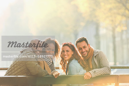 Portrait smiling young couple friends on sunny autumn bench
