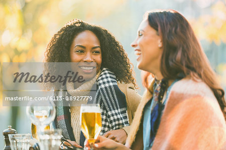 Smiling young women friends drinking beer at autumn sidewalk cafe