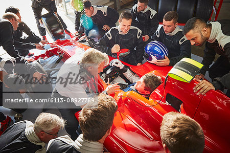 Manager and pit crew surrounding formula one driver in race car