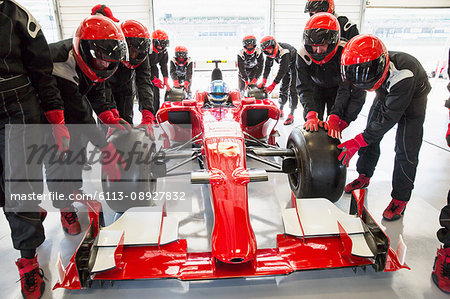 Pit crew pushing formula one race car into repair garage