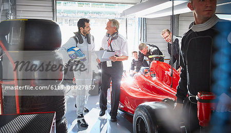 Manager and formula one race car driver talking in repair garage