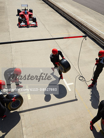 Pit crew preparing tires for nearing formula one race car in pit lane