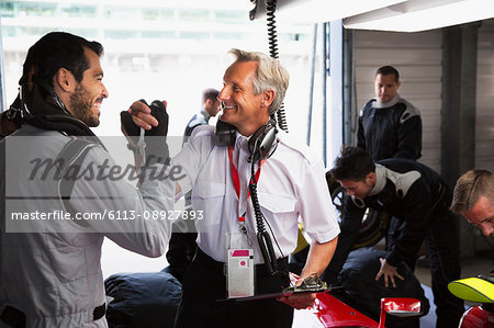 Manager and formula one driver celebrating, handshaking in repair garage