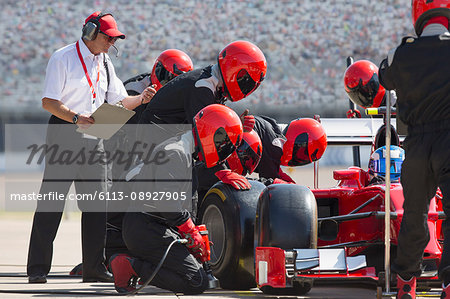 Manager with stopwatch timing pit crew replacing formula one race car tire in pit lane