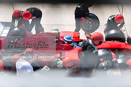 Manager with stopwatch timing pit crew replacing tires on formula one race car in pit lane