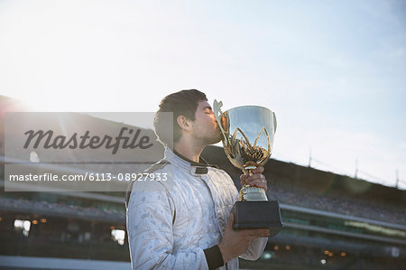 Male formula one driver kissing trophy, celebrating victory on sports track