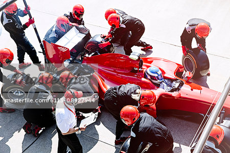 Manager with stopwatch timing pit crew replacing tires in pit lane