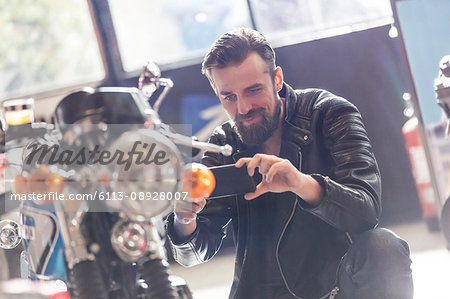 Man with camera phone photographing motorcycle in shop