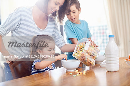 Mother pouring cereal for daughter at breakfast table