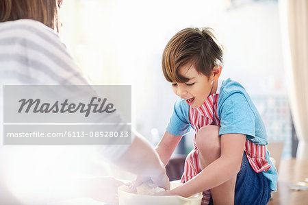 Smiling boy helping mother baking, mixing dough in bowl