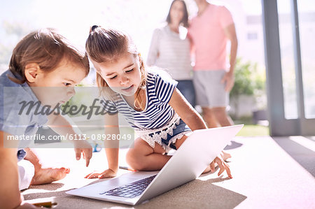 Brother and sister using laptop on sunny floor