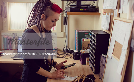 Female hairdresser using mobile phone and making notes in dreadlocks shop