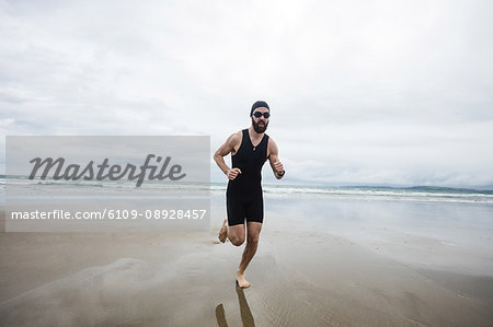 Man in swimming costume and swimming cap running on beach