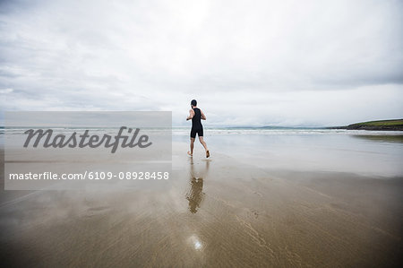 Rear view of man in swimming costume and swimming cap running on beach