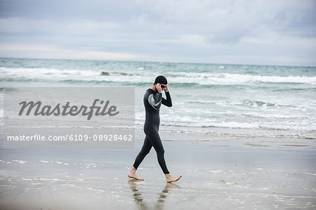 Athlete in wet suit wearing swimming goggles while walking on the beach