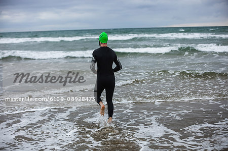Rear view of athlete in wet suit running towards the sea