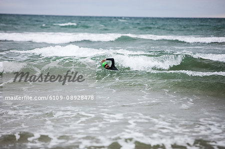 Man in wet suit swimming in sea on beach