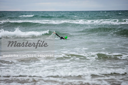 Man in wet suit swimming in sea on beach