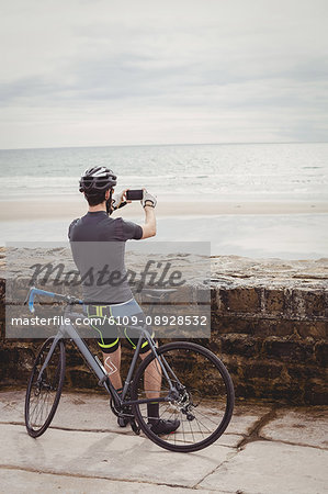 Rear view of athlete clicking a picture from his smartphone while resting on his bicycle
