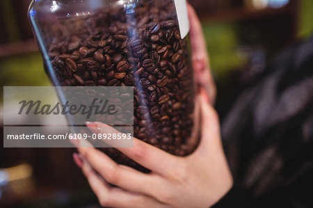 Close-up of woman holding jar of coffee beans at counter in shop
