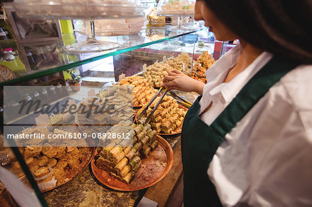 Female shopkeeper arranging turkish sweets at counter in shop